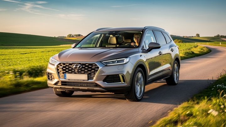 SUV familial circulant doucement sur une route de campagne ensoleillée, avec une conductrice attentive visible à travers le pare-brise.