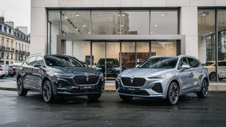 Deux SUV premium et sportifs à motorisation thermique stationnés devant une concession automobile française moderne, photographiés dans un style journalistique réaliste.
